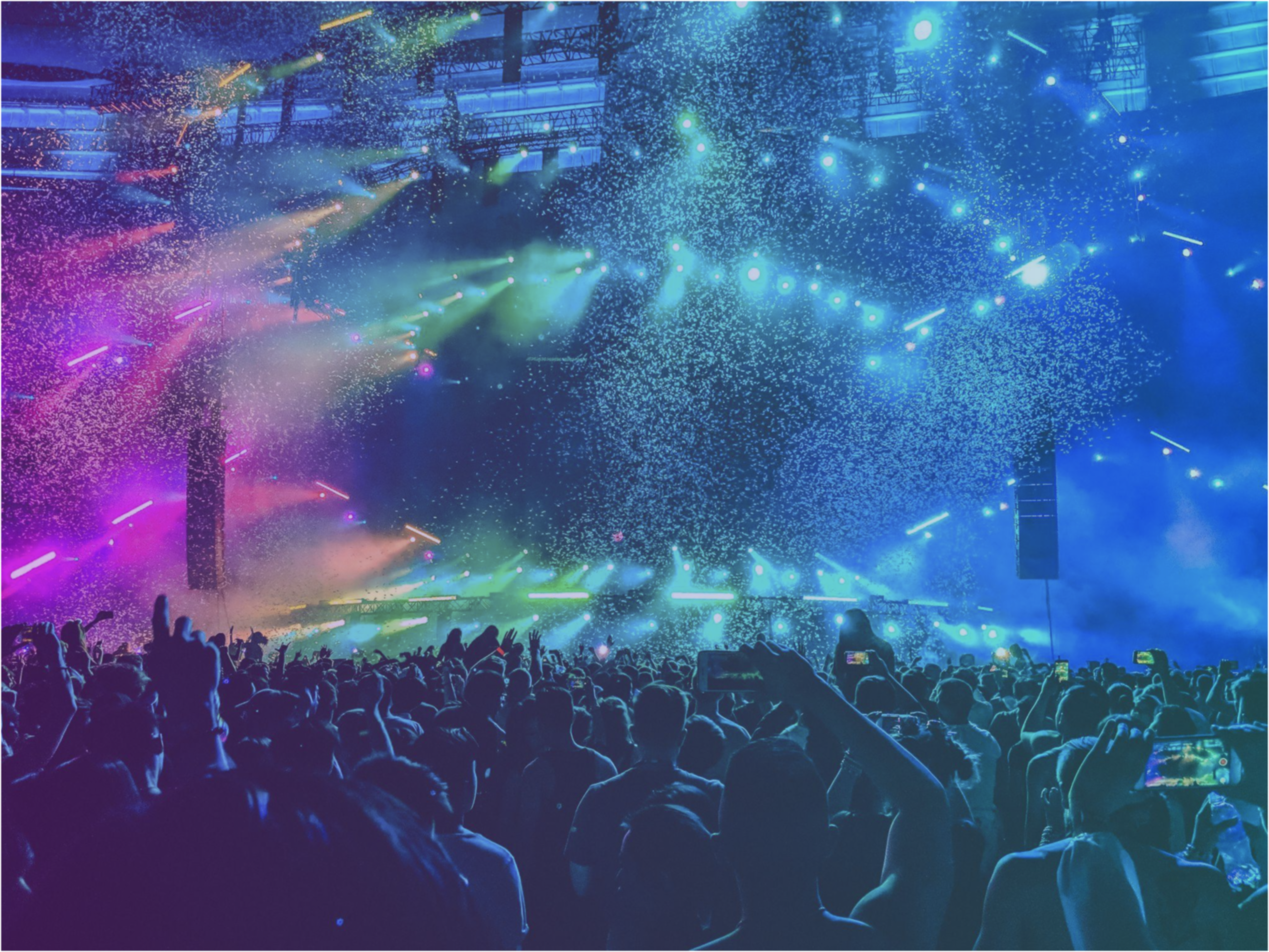 A festival crowd in front of a stage lit with colored light